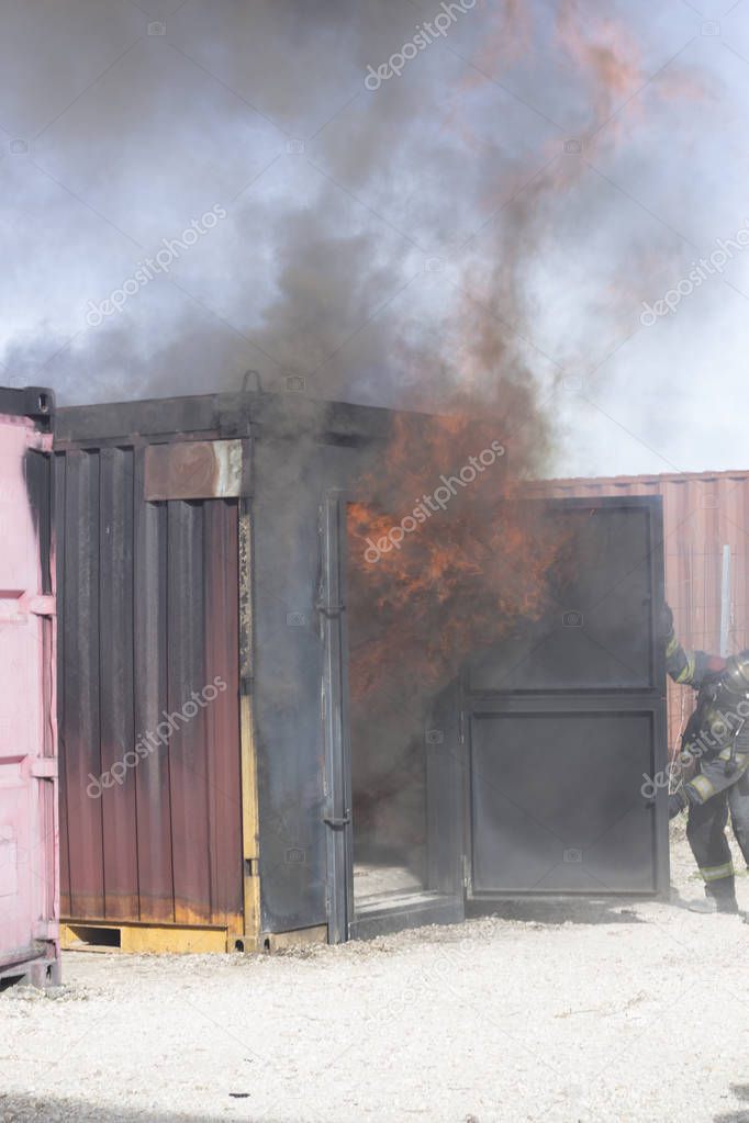 Firefighter putting out fire training station extinguisher backdraft emergency safety drill with ship container.