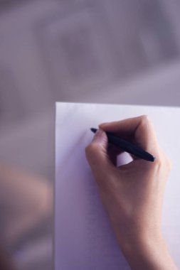 Masada elinde kalemle kağıda yazan genç bayan..