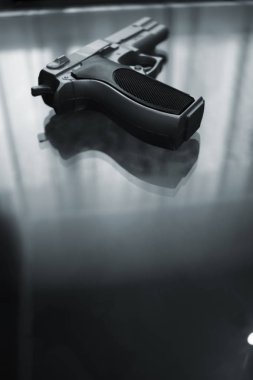 Otomatik tabanca silah siluet pencere ışık yansıması ile daki lüks otel yatak odasında cam masa üzerinde.