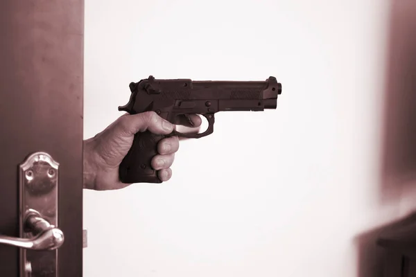 Hand holding automatic pistol gun in bedroom in luxury hotel in silhouette with window light.