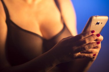 Seksi büyük göğüslü kadın erotik iç çamaşırlarıyla cep telefonu kullanıyor..