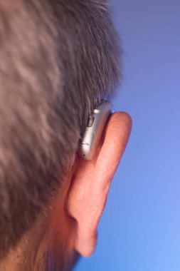 Kafkasyalı beyaz yaşlı adam kulağına modern dijital işitme cihazı takıyor ve gri saçlı..