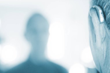 Kafkasyalı beyaz yaşlı adam kulağına modern dijital işitme cihazı takıyor ve gri saçlı..