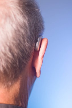 Kafkasyalı beyaz yaşlı adam kulağına modern dijital işitme cihazı takıyor ve gri saçlı..