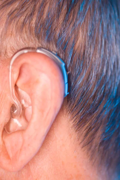 Caucasian white old aged man wearing modern digital hearing aid in ear with grey hair.