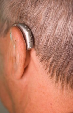 Kafkasyalı beyaz yaşlı adam kulağına modern dijital işitme cihazı takıyor ve gri saçlı..