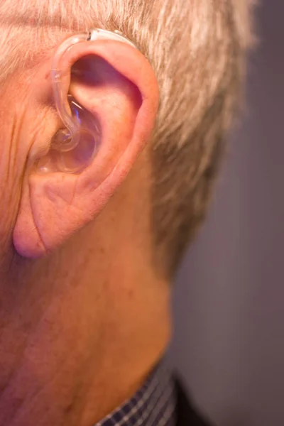 Caucasian white old aged man wearing modern digital hearing aid in ear with grey hair.