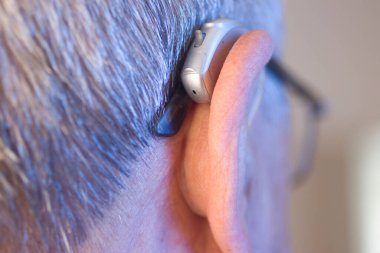 Kafkasyalı beyaz yaşlı adam kulağına modern dijital işitme cihazı takıyor ve gri saçlı..