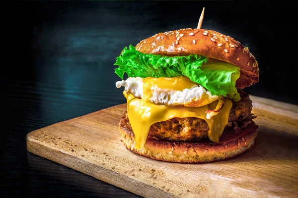 Homemade meat burgers with egg, sauce and vegetables on a dark background. Egg burger