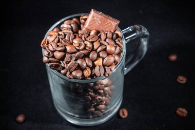 Cam fincan kahve kahve çekirdekleri ve karanlık bir arka plan üzerinde çikolata ile yakın çekim, düşük bir anahtar.