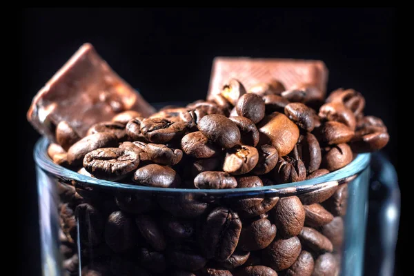 Tasse en verre de café avec grains de café et chocolat sur un fond sombre, gros plan dans un discret — Photo