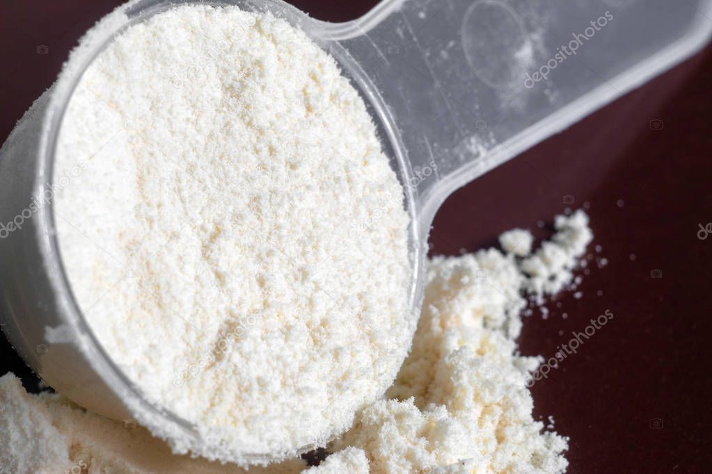 Plastic measuring spoon and heap of protein powder dark background. Top view