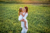 Mutter und Tochter umarmen sich im Sonnenuntergang auf der grünen Wiese
