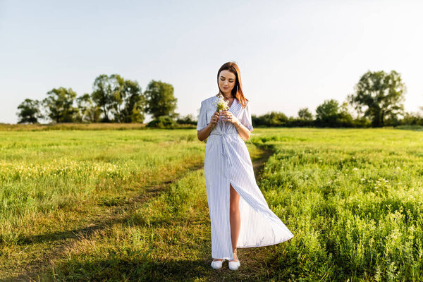 привлекательная молодая женщина в белом платье с букетом полевых цветов на зеленом поле
