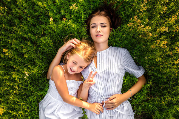 top view of mother and daughter lying in flowery meadow and looking at camera
