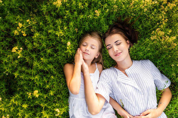 top view of happy mother and daughter relaxing while lying in flowery meadow