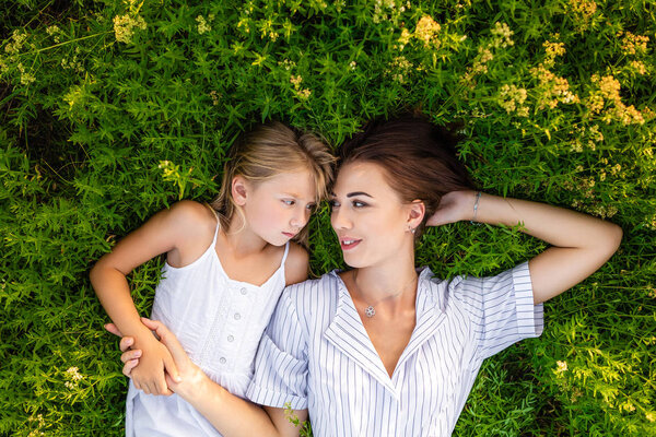 top view of mother and daughter relaxing while lying in flowery meadow and looking at each other