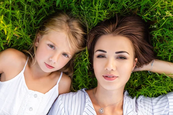 top view of mother and daughter lying on green grass and looking at camera