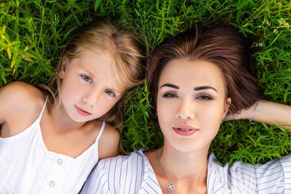 top view of mother and daughter lying on green grass and looking at camera