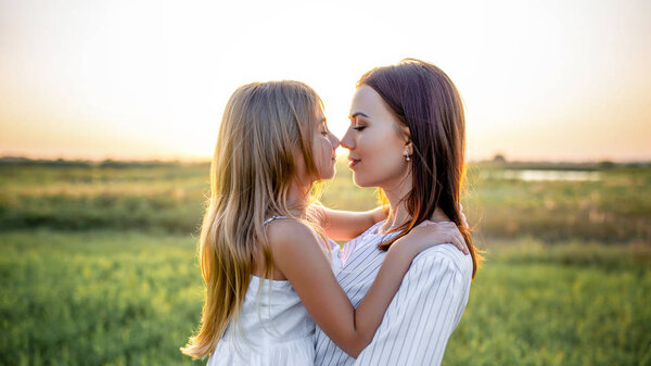 close-up portrait of mother and daughter embracing and touching noses in green field on sunset