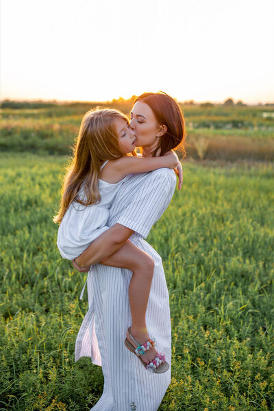 mother and daughter embracing in green field on sunset