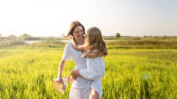美丽幸福的母亲和女儿拥抱在绿色的田野上日落 — 图库照片
