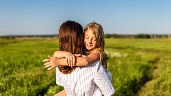 mother embracing with her happy daughter in green meadow