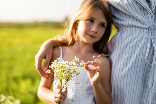 被裁剪的母亲拥抱女儿 而她拿着田野鲜花花束在绿色的草地上拍摄 — 图库照片