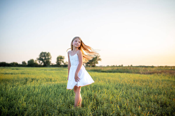adorable little child in white dress posing on field on sunset