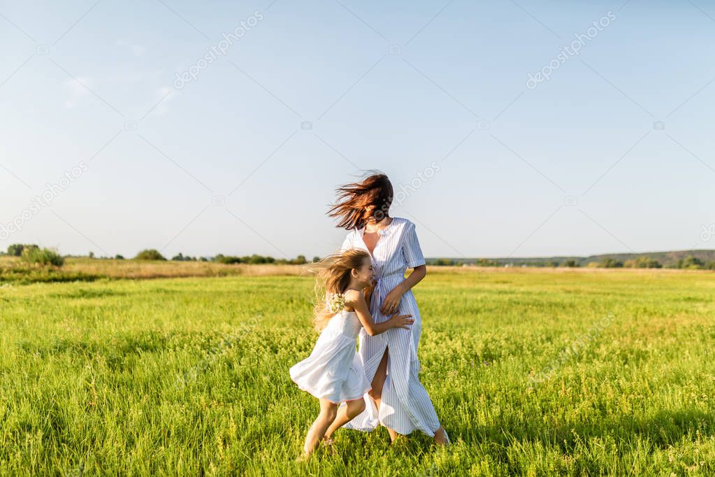 mother and daughter having fun together and embracing in green meadow on windy day