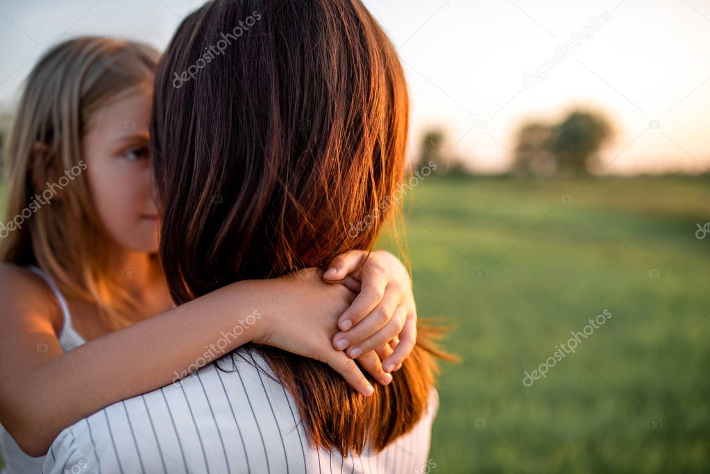 mother and daughter embracing in green meadow on sunset