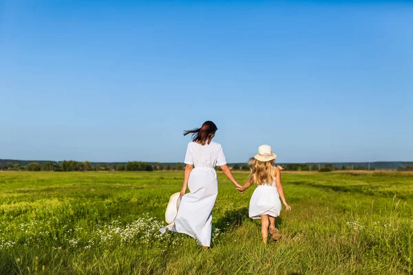 Vue arrière de la mère et de la fille marchant ensemble par champ vert le jour ensoleillé — Photo de stock