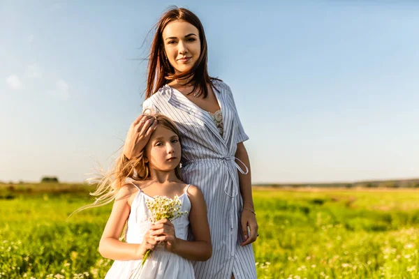 Mother and daughter in white dresses looking at camera together in green field — Stock Photo