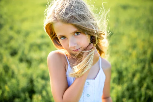 Primer plano retrato de lindo niño en vestido blanco posando en el campo verde y mirando a la cámara - foto de stock