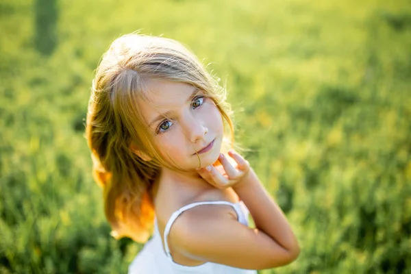 Close-up portrait of beautiful little child in white dress posing in green field and looking at camera — Stock Photo