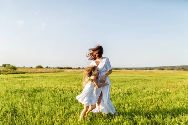 Mother and daughter having fun together and embracing in green meadow on windy day — Stock Photo