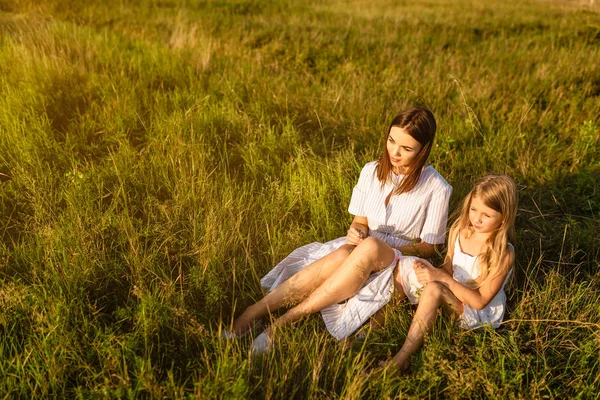 Madre e hija sentadas sobre hierba verde y mirando el atardecer - foto de stock