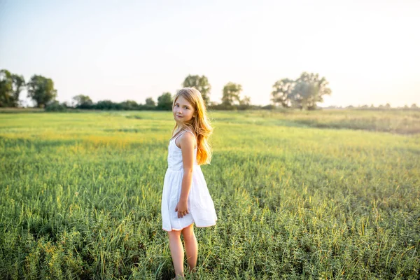 Nettes kleines Kind im weißen Kleid posiert auf der grünen Wiese und blickt in die Kamera — Stockfoto
