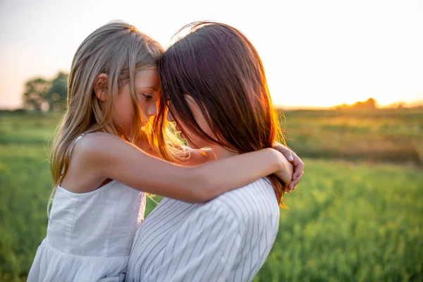 Retrato de cerca de la madre y la hija abrazándose en el campo verde al atardecer - foto de stock