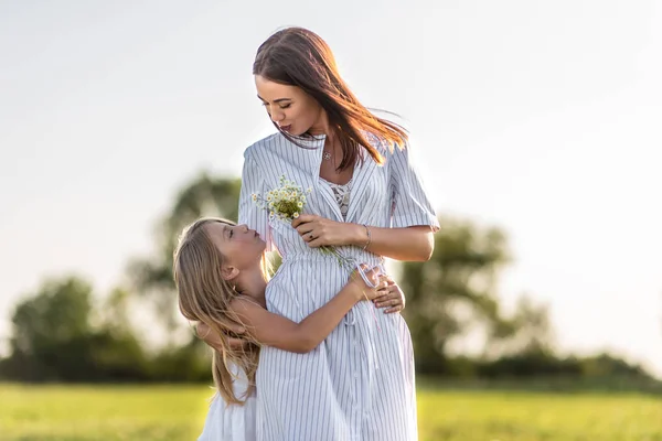 Madre e hija con ramo de flores de campo abrazándose en el prado verde - foto de stock