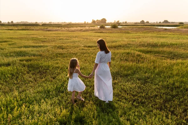Rückansicht von Mutter und Tochter, die abends auf einer grünen Wiese spazieren gehen — Stockfoto