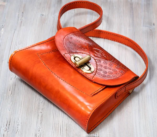 handmade orange toned embossed leather handbag on gray wooden table