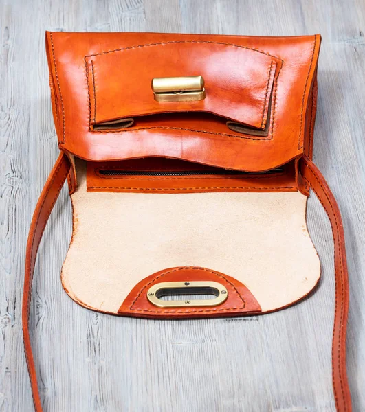 handmade empty orange colored leather bag on gray wooden table