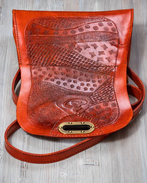 back side of open handmade orange colored embossed leather handbag on gray wooden table