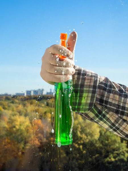 man sprays the washing liquid on glass to clean a home window in sunny autumn day