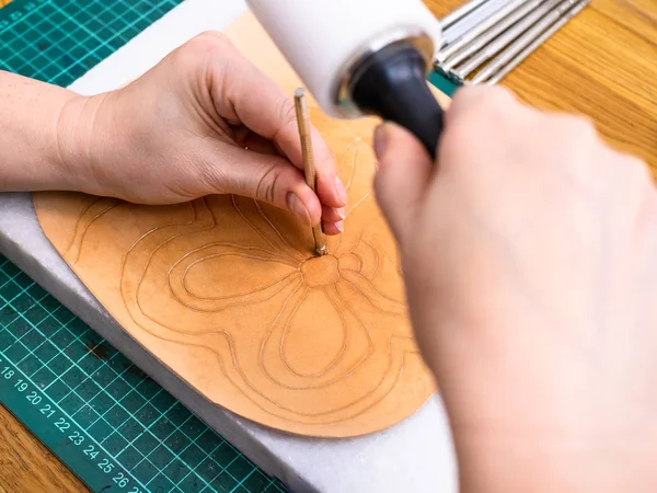 workshop of making the carved leather bag - craftsman stamps the floral ornament on surface of rough vegetable tanned leather with Stamping tool and mallet