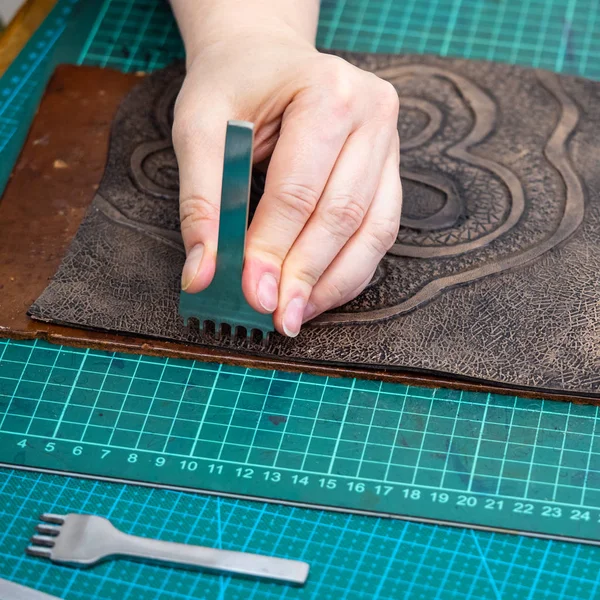 workshop of making the carved leather bag - craftsman punches edge of decorative item for handbag by stitching punch