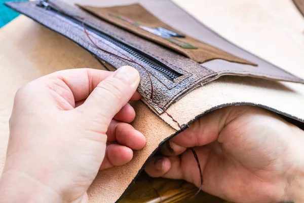 workshop of making the carved leather bag - craftsman stitches the inner pocket in leather handbag by needle with thread