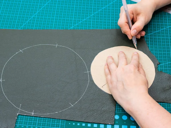 workshop of making the leather bag for jewelry - craftsman draws cutting pattern of the pouch using paper shape