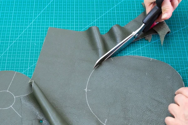 workshop of making the leather bag for jewelry - craftsman cuts the bottom of pouch from sheet of leather using drawn sketch